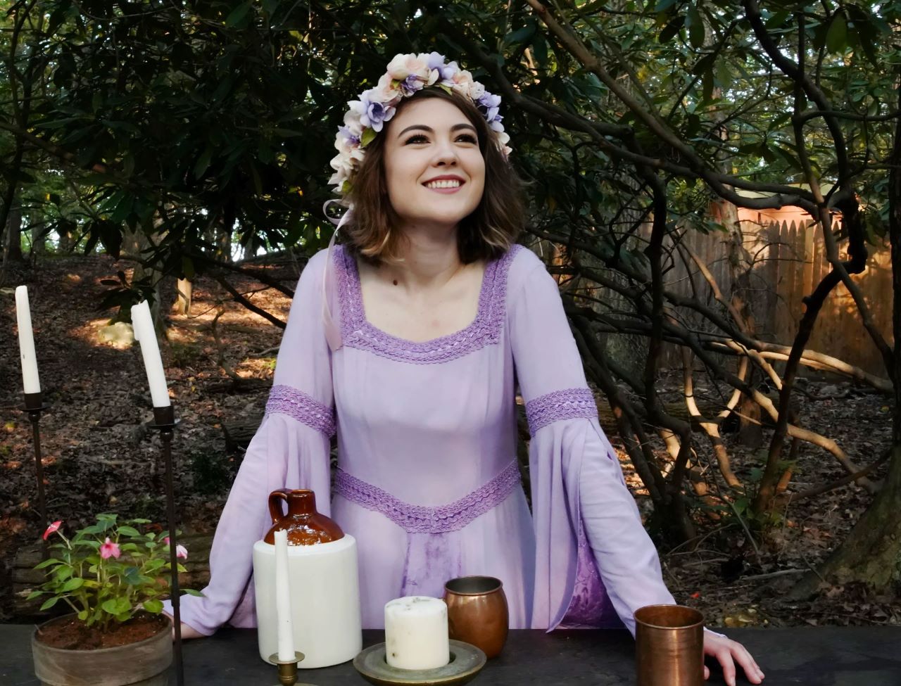 woman wearing purple renaissance dress while leaning on a wooden table