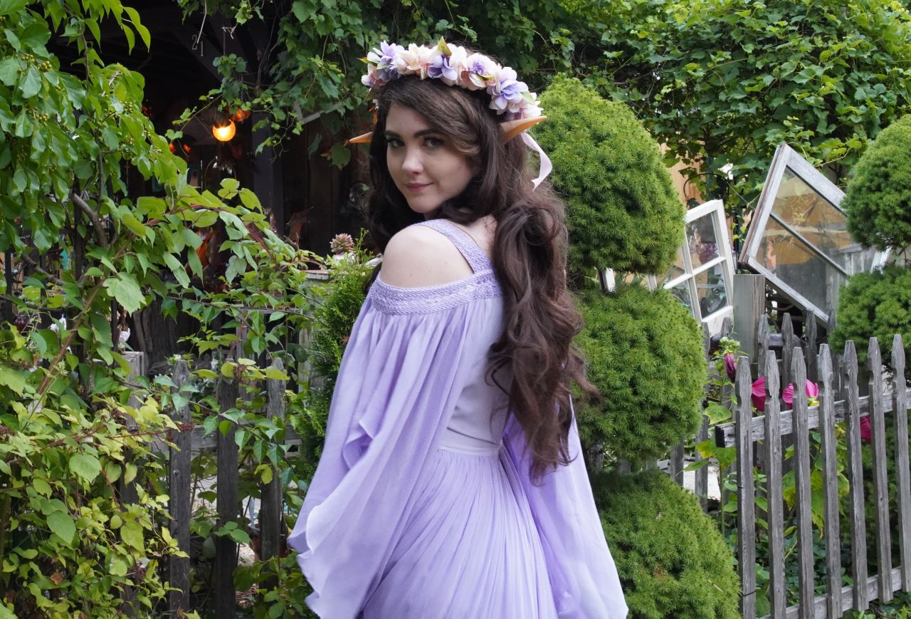 Woman in lavender off-shoulder medieval dress with floral crown and elf ears in garden