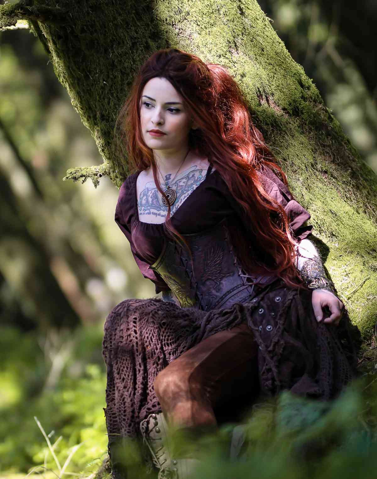 pretty woman with tattoo on her chest leaning on a tree in the woods