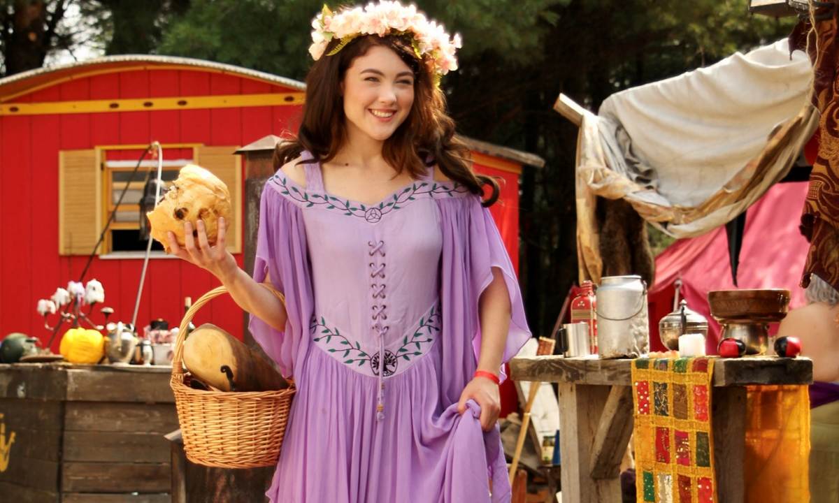 young woman wearing purple renaissance dress while holding a bread and a basket