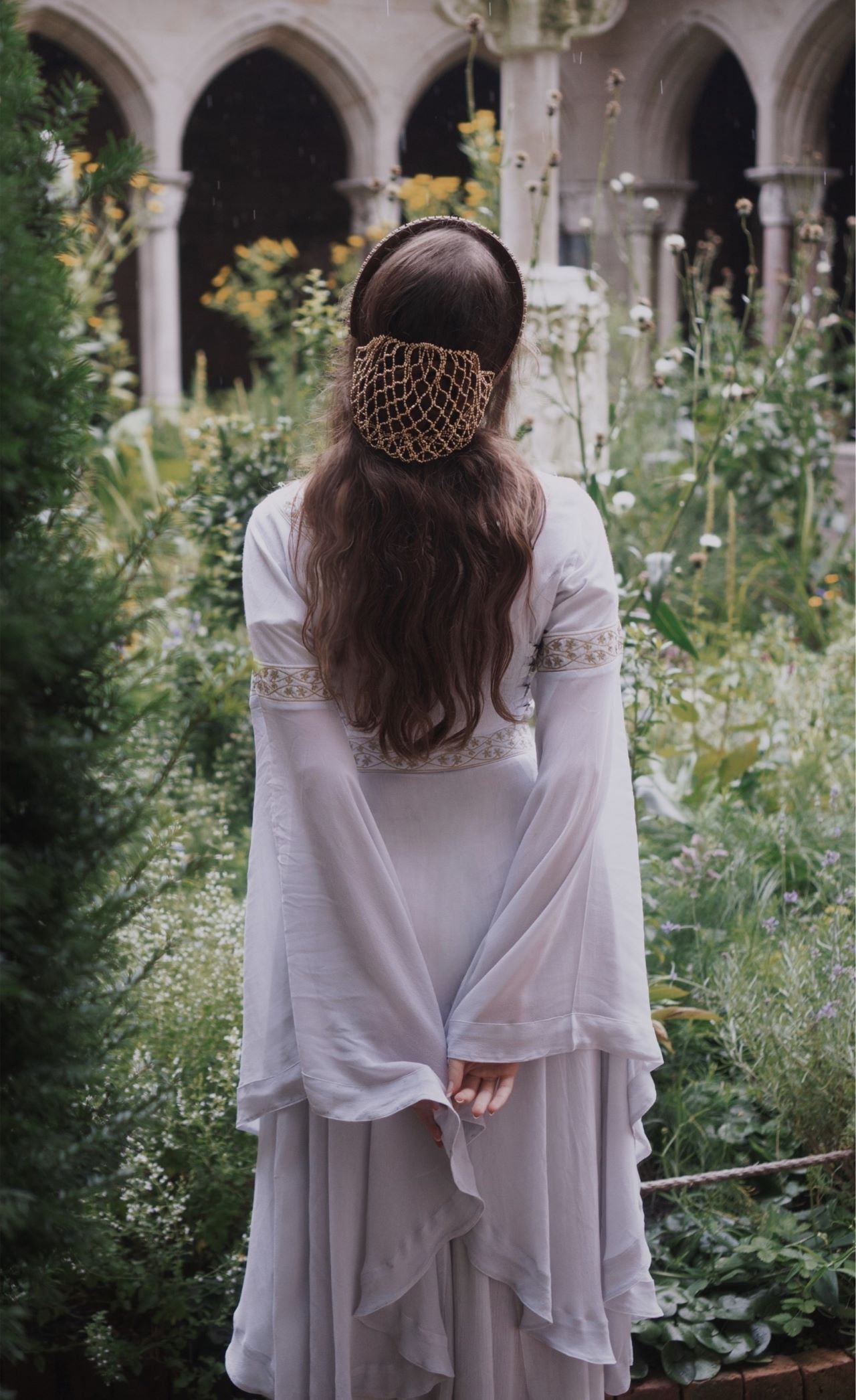 Woman in White medieval bell-sleeve dress with gold snood in Gothic garden